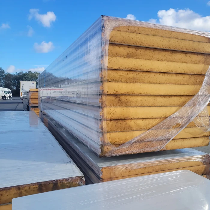 Chantier extérieur avec panneaux sandwich isolants empilés sous film plastique de protection