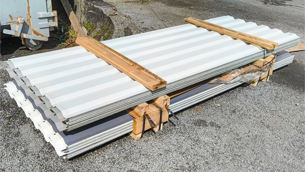 Chantier extérieur avec panneaux sandwich isolants blancs empilés sur palette bois, sécurisés par sangles