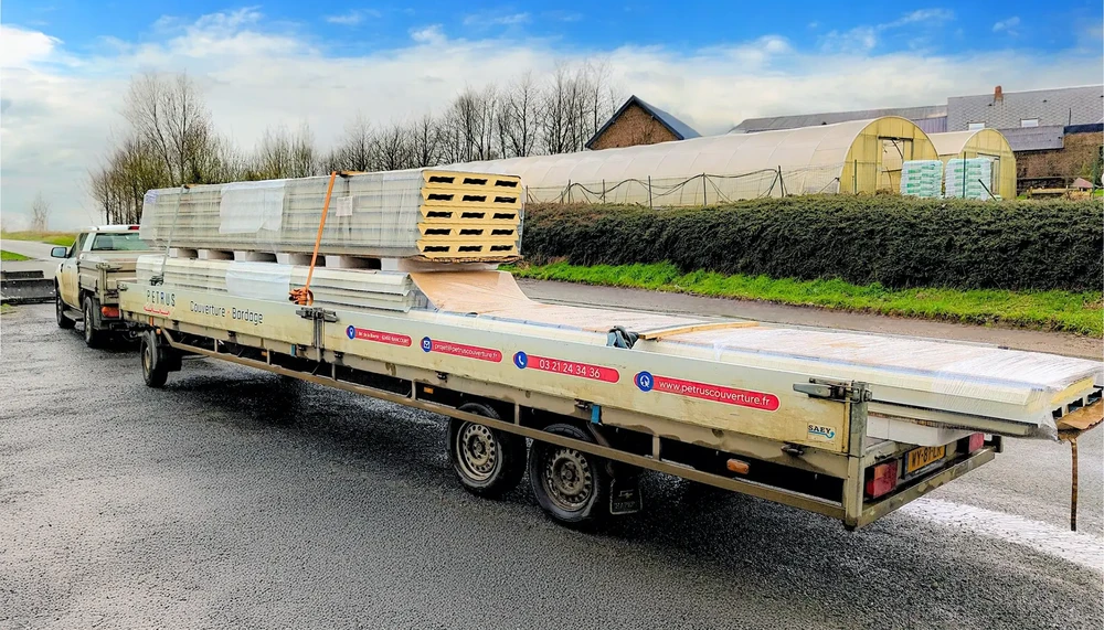 Chantier extérieur avec camionnette tractant une remorque plateau porte-engins chargée de matériaux de construction