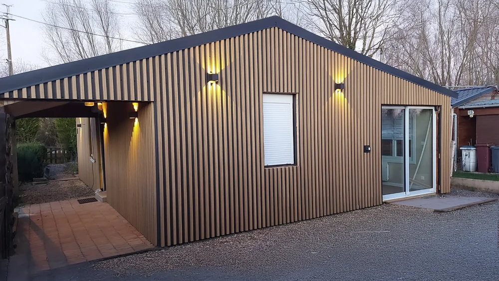 Un artisan menuisier travaille dans un atelier intérieur, assemblant une structure triangulaire en bois massif sur sol béton